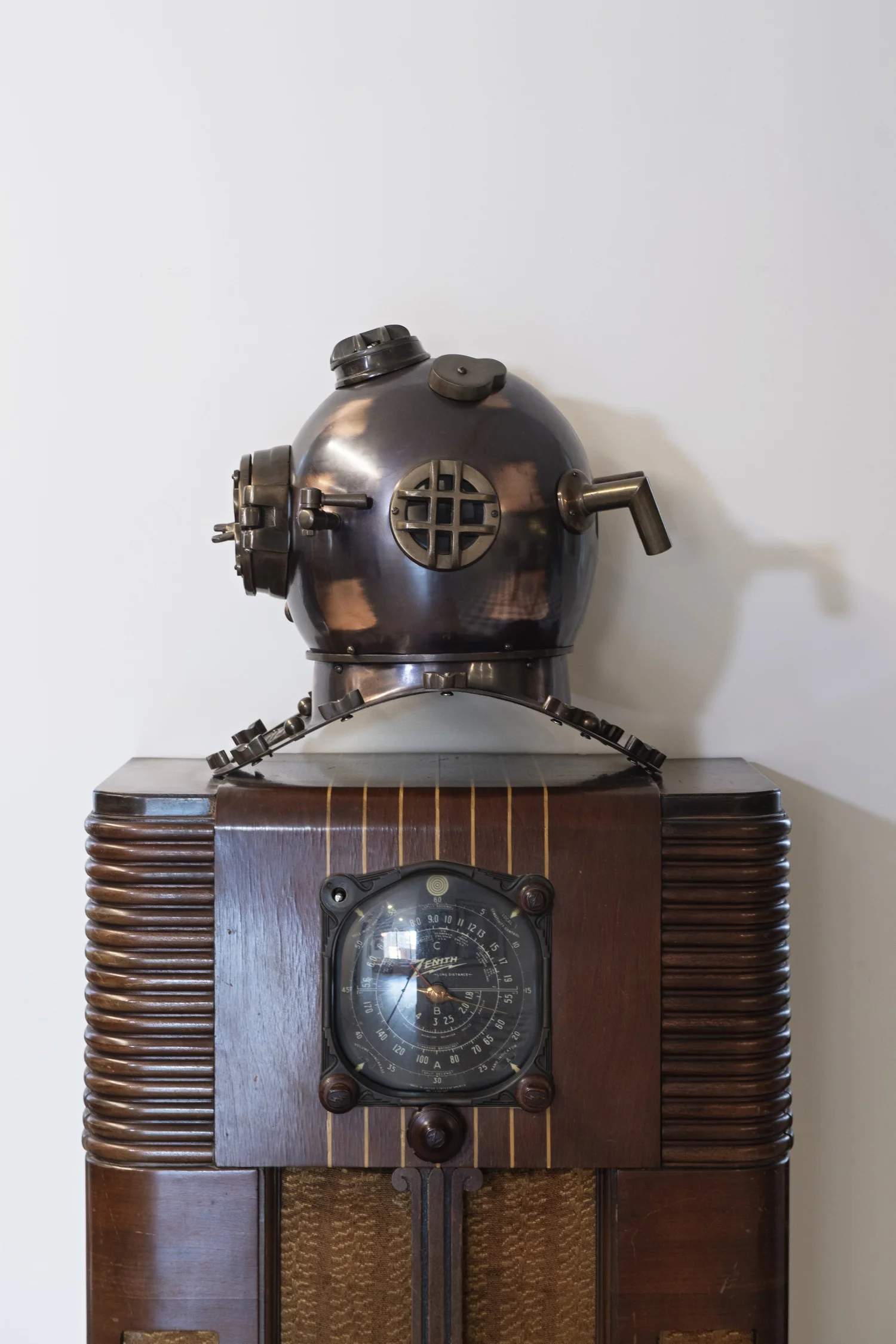 Antique brass diving helmet resting on a wooden Zenith radio
